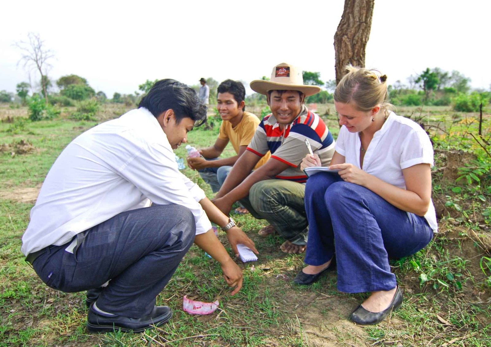 Alexandra Hiniker crouching in a field with local residents, taking notes as they talk
