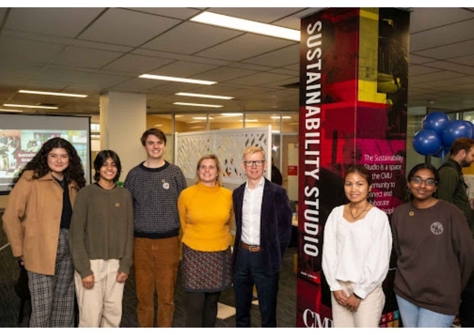 Alexandra Hiniker standing with a group of students and a university dean beside a pillar labelled Sustainability Studio