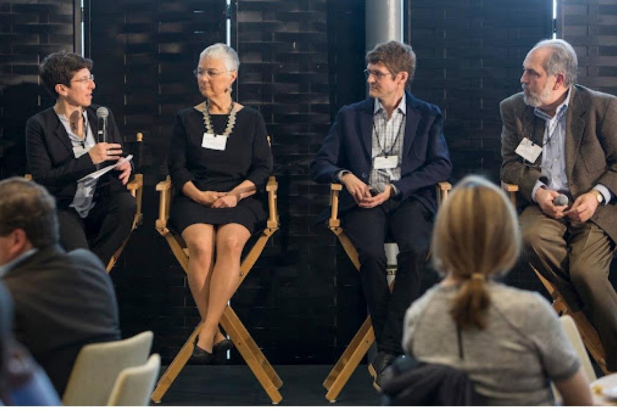 Julie Newman speaking into a microphone on a panel of four speakers seated on director's chairs at the Sustainability Connect forum at MIT