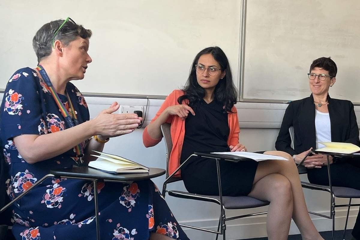 Julie Newman seated on the right of a three person panel, listening as a fellow panellist speaks and gestures