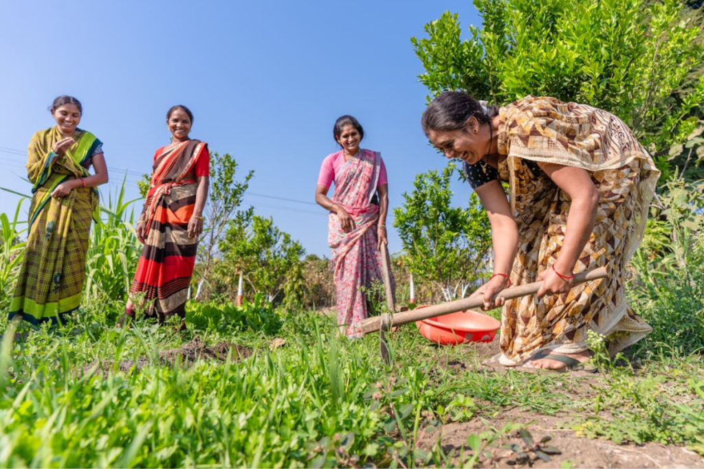 A group of cheerful Indian women farmers in colorful sarees working together in a field, symbolizing the empowerment and well-being of smallholder farmers in India's agricultural sector