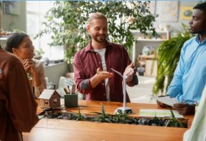 A business team discusses sustainable practices by examining a model wind turbine, representing a commitment to renewable energy.
