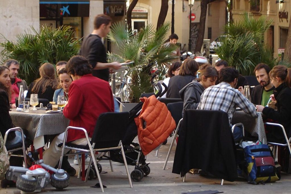 A group of people dining and socializing at an outdoor cafe in a pedestrian-friendly urban plaza, likely a "Superblock."