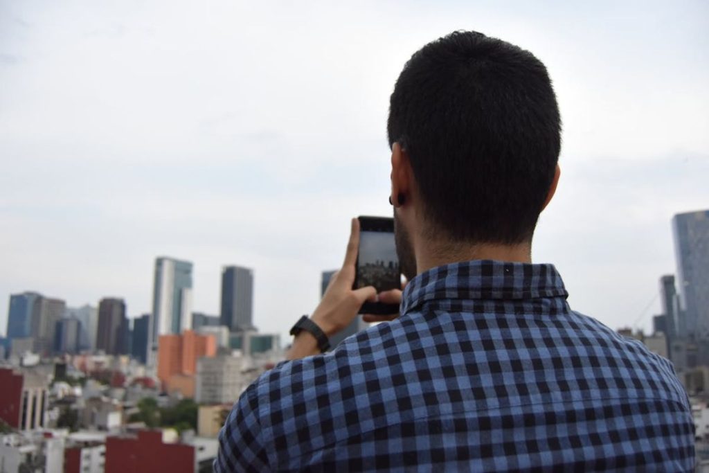 A man from behind, using his smartphone to photograph a modern city skyline, symbolizing the "smart citizen."