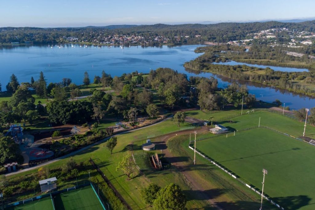 An aerial view of a large, green urban park with sports fields and a lake, demonstrating nature-based solutions for climate resilience.