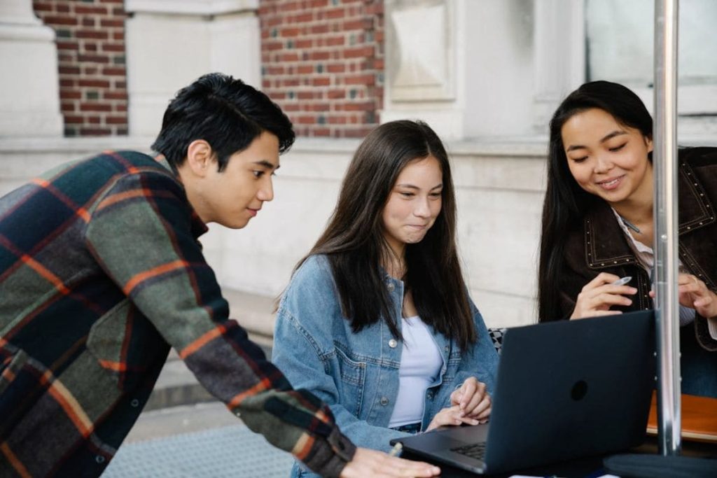 Three diverse students collaborating on a laptop, researching topics central to the mission of Earth5R.