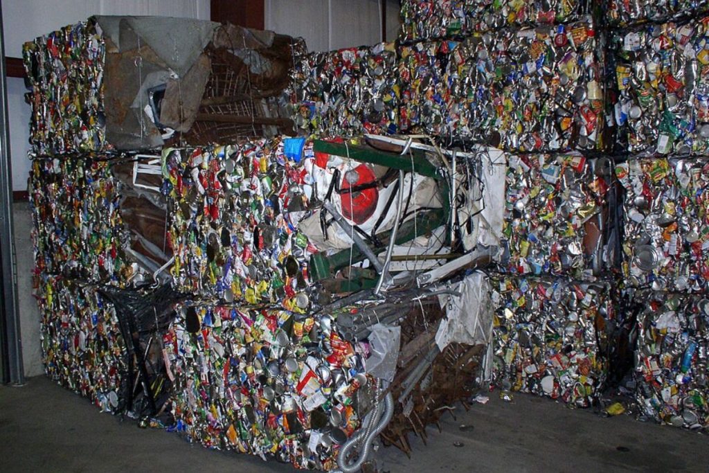 Bales of compressed, mixed recyclable waste, predominantly metal cans, stacked high in a facility, representing the industrial scale of material recovery in effective waste management systems for circularity.