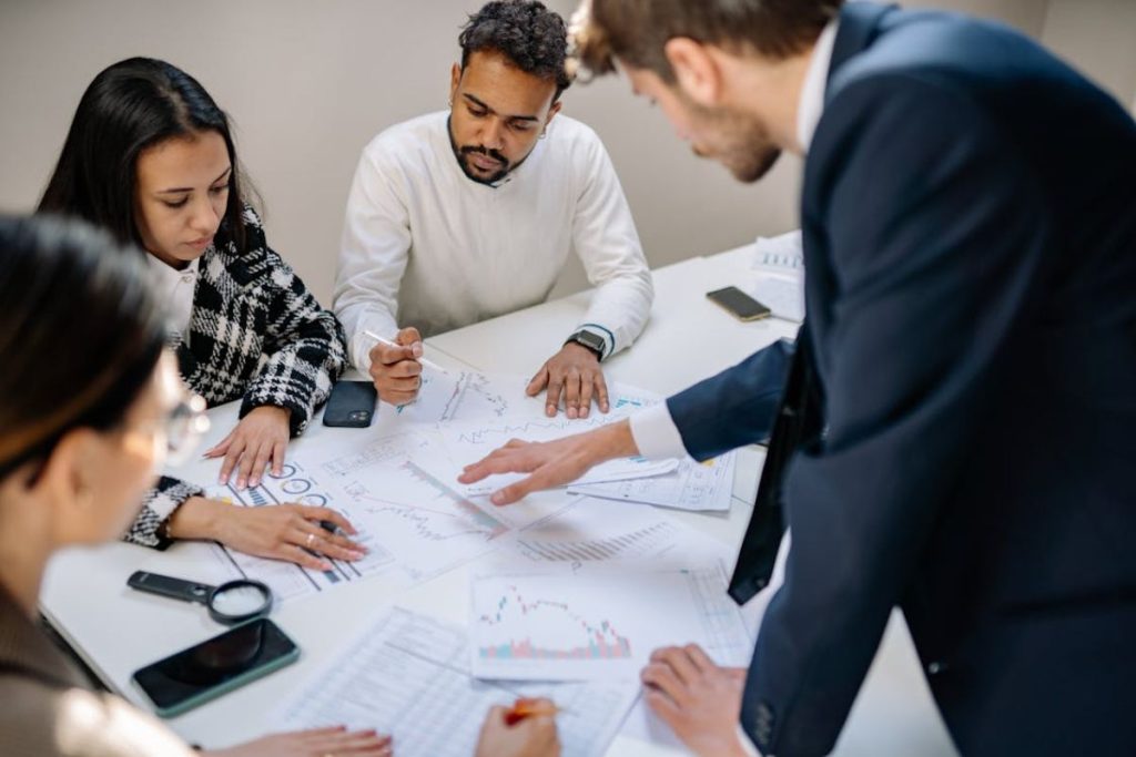 A diverse group of colleagues leans over a table, analyzing charts and data together, demonstrating the collaborative, research-driven side of corporate sustainability.