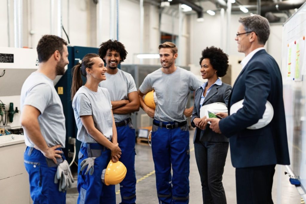 Diverse group of employees, including a manager and factory workers, discussing employee-led sustainability initiatives in a corporate setting.