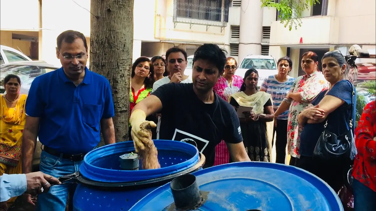 Saurabh Gupta of Earth5R adding segregated kitchen waste to a blue drum composter while housing society residents in Mumbai watch