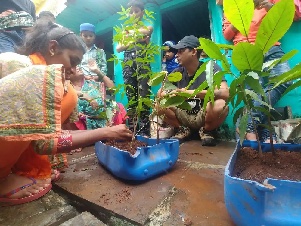 Residents planting saplings in upcycled blue containers filled with compost made from zero waste buildings in Mumbai