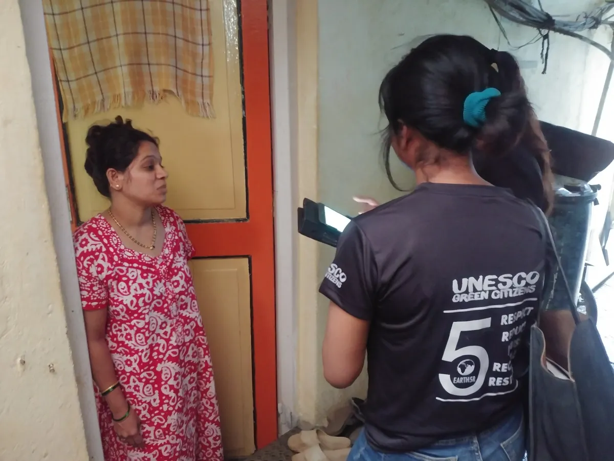 Earth5R volunteer in a UNESCO Green Citizens t-shirt explaining wet and dry waste segregation to a resident at her doorstep in Mumbai