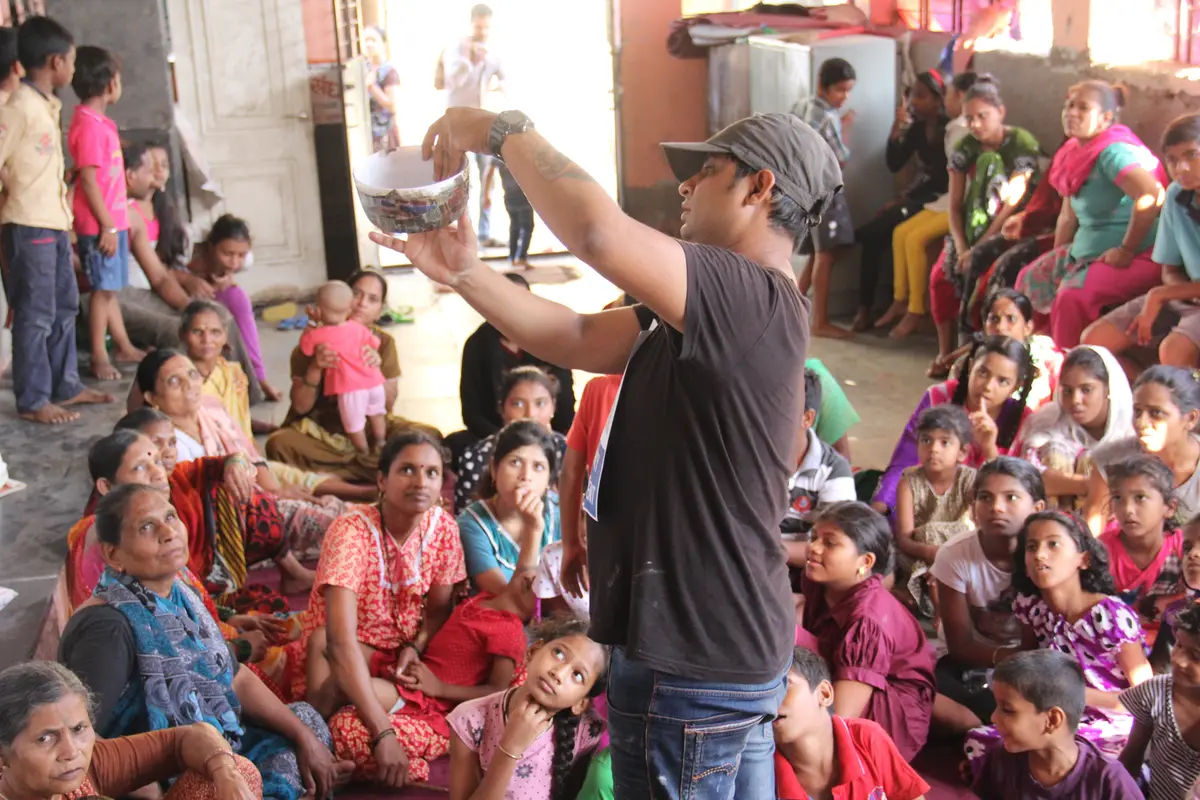 Earth5R facilitator holding up an upcycled paper bowl in front of a large audience of children and women