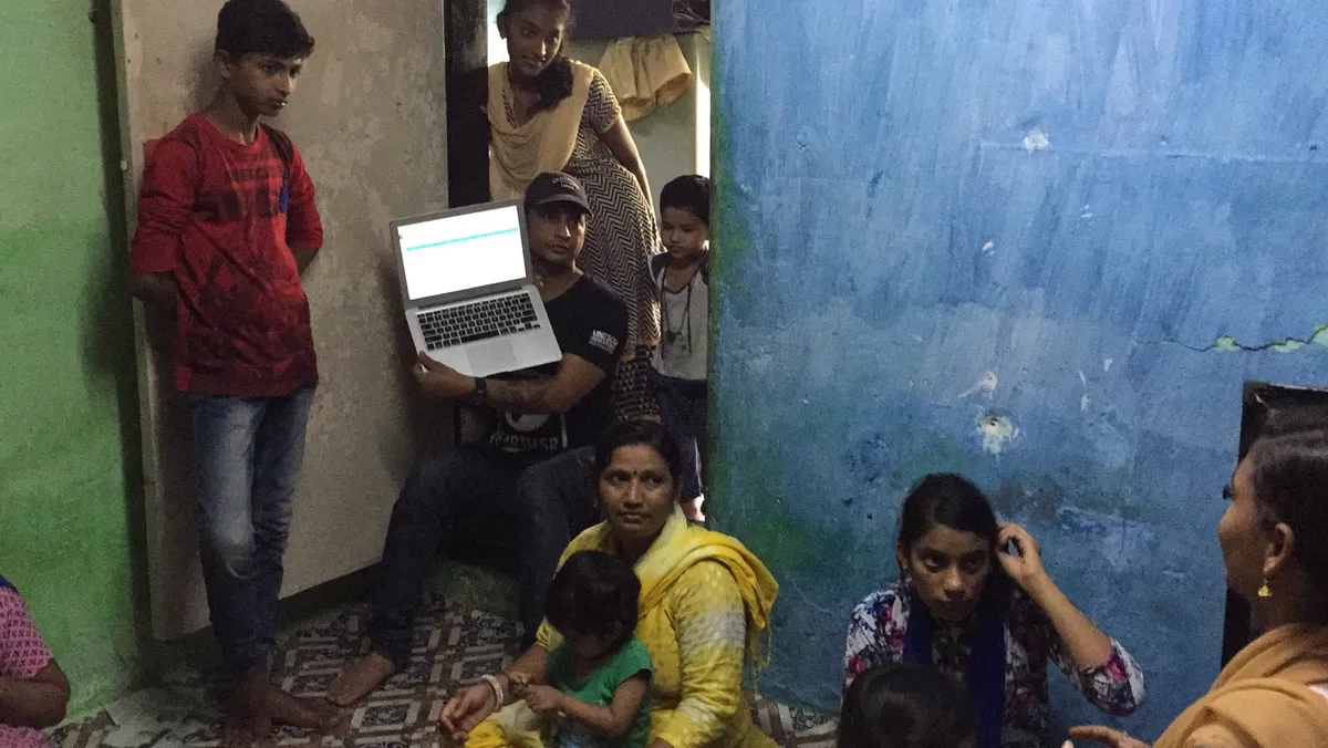Earth5R volunteer showing livelihood and circular economy videos to slum residents on a laptop