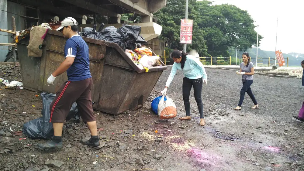 Hexaware employees clearing litter around a riverside waste bin during the Earth5R cleanup in Pune