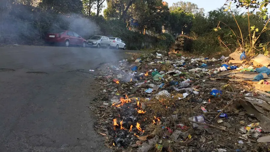 Pile of mixed garbage burning by a roadside, with smoke rising