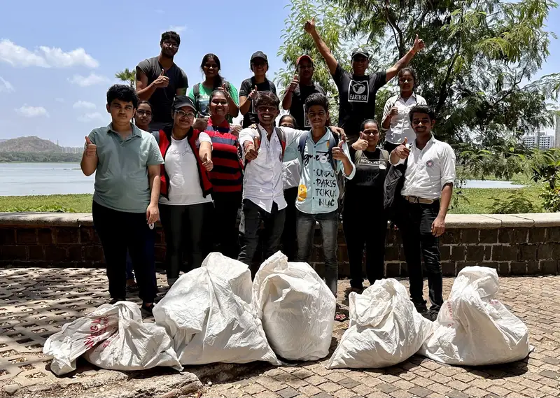 Student volunteers celebrating beside bags of waste collected at the Powai Lake cleanup, Earth5R CSR programme in Mumbai