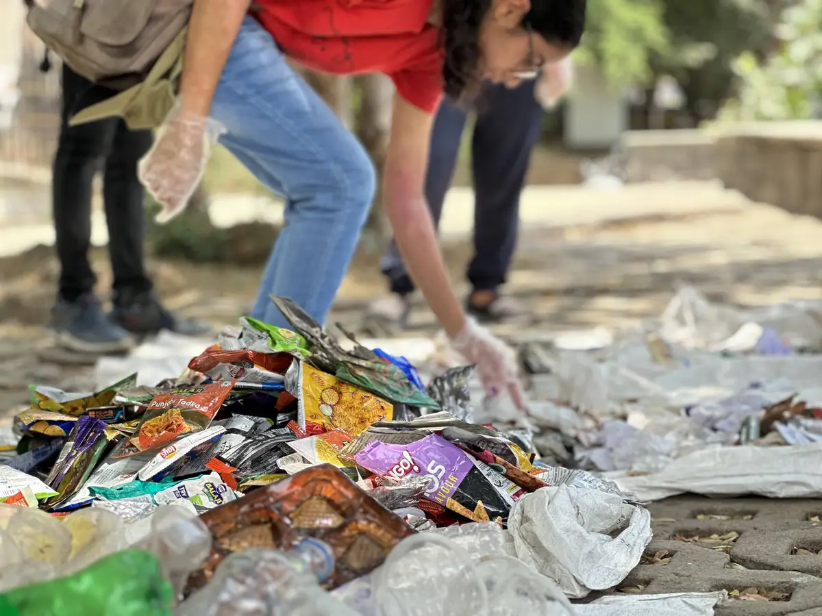 Volunteer examining plastic wrappers for a brand and waste study at the Powai Lake cleanup, Earth5R CSR programme in Mumbai