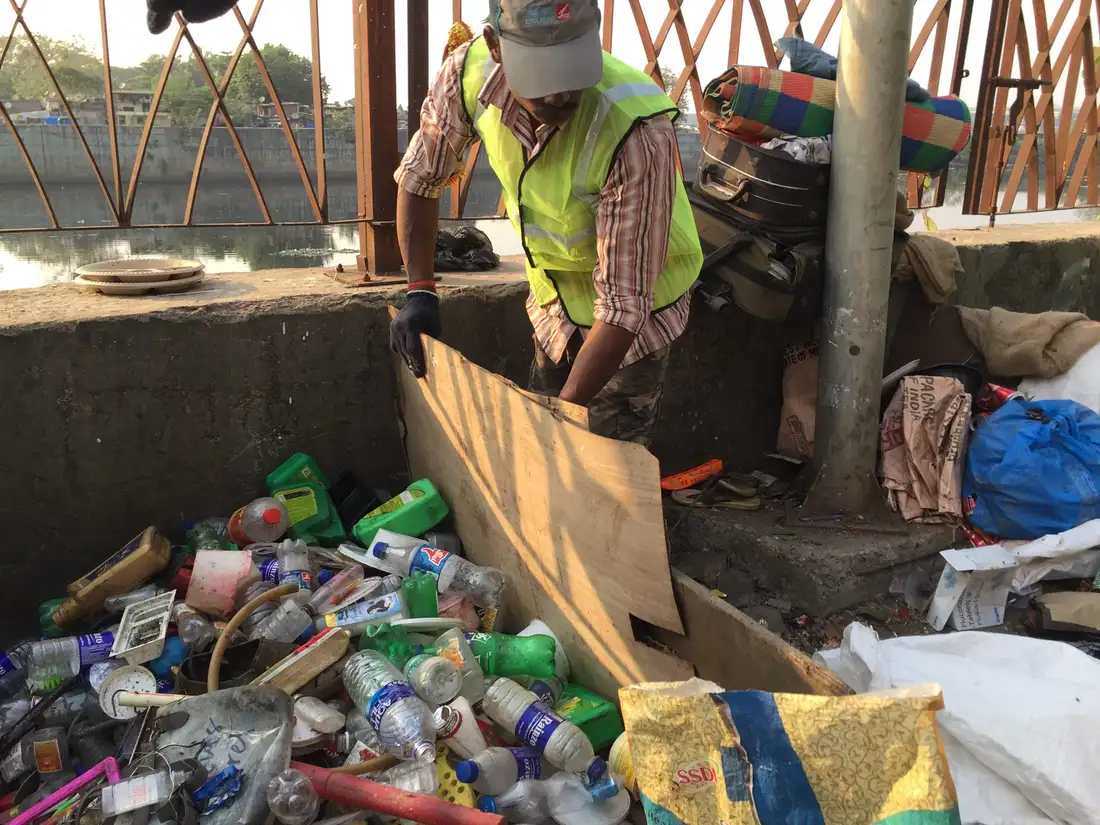 Waste collector recovering plastic bottles from the Mithi River bank during Earth5R plastic recovery work in Mumbai