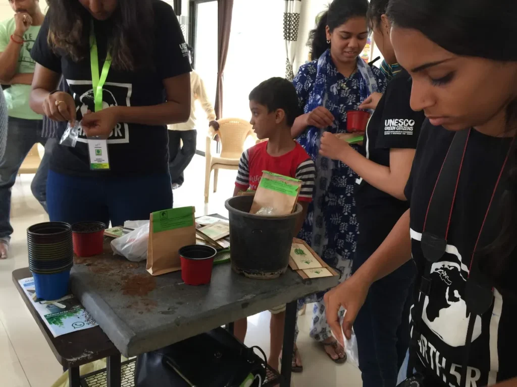 Earth5R volunteers Sonam Sengar, Shriyam Jalan, Manasi teaching children and parents to pot saplings with compost