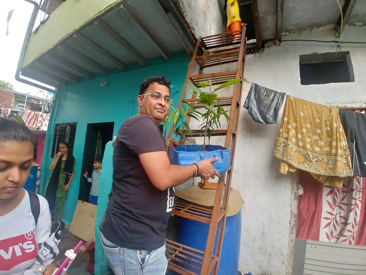Earth5R volunteer carrying an upcycled planter up to a tin rooftop in an informal settlement in Mumbai