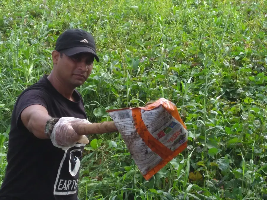 Earth5R volunteer holding a multilayer plastic wrapper found in vegetation beside Powai Lake, Mumbai