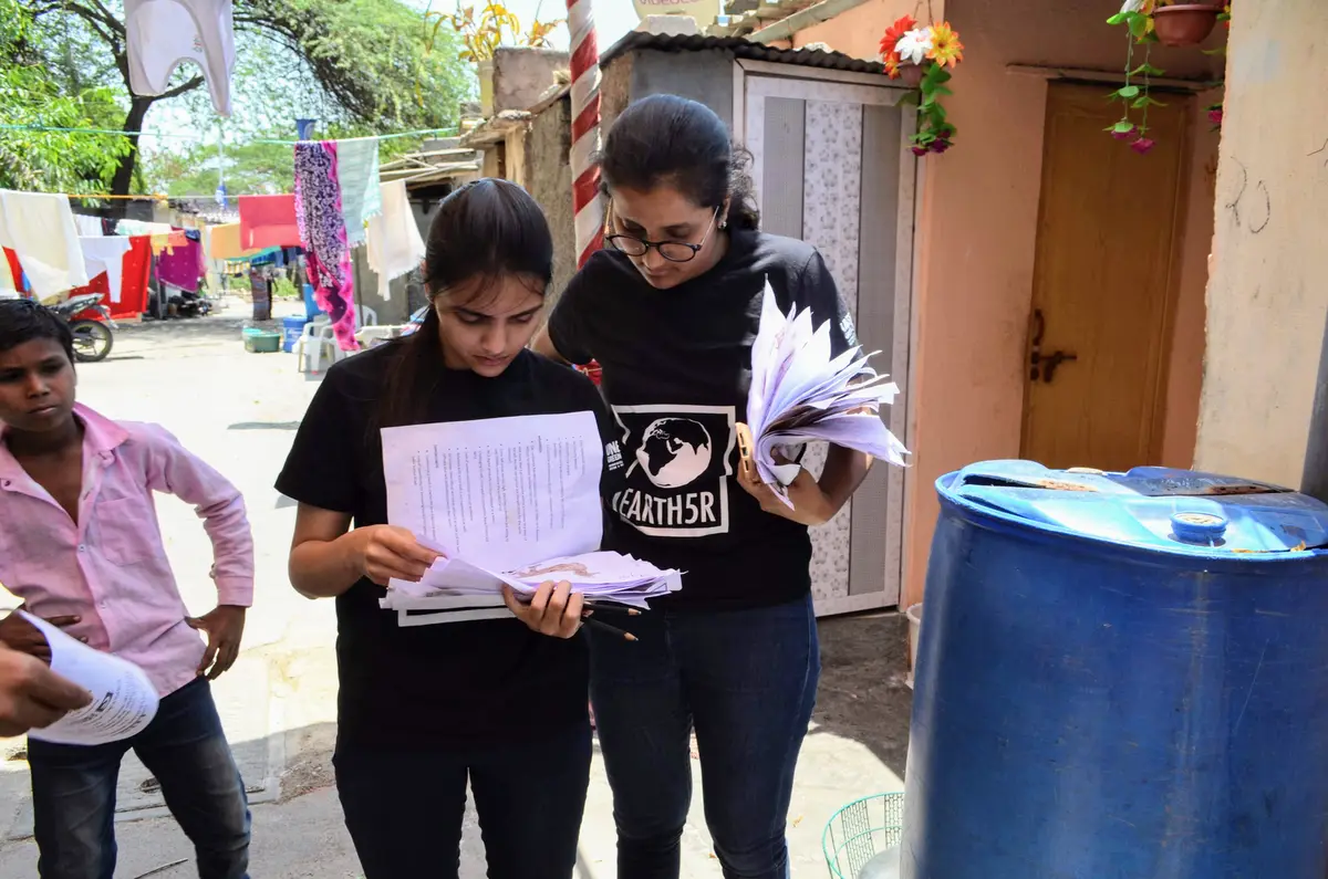 Earth5R volunteers reviewing household survey forms beside a water drum in a settlement