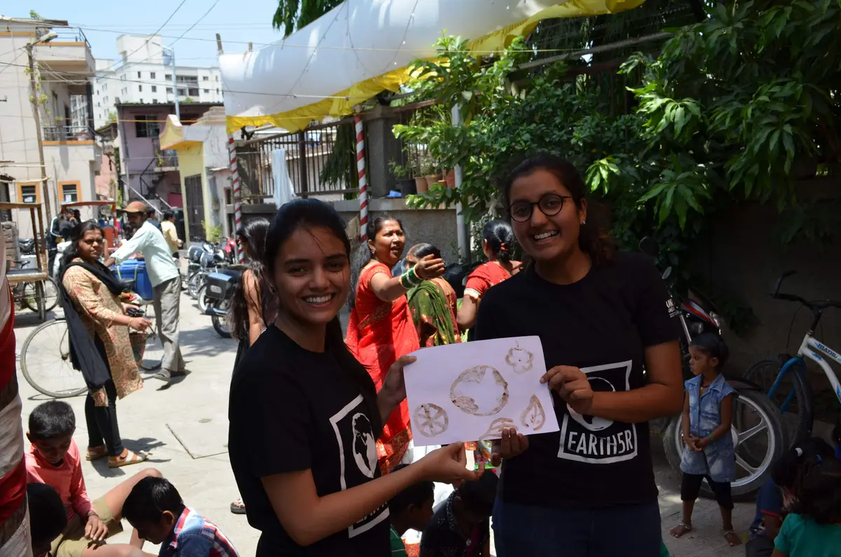 Two Earth5R volunteers holding up a 5R activity sheet with residents in the background, Earth5R CSR programme