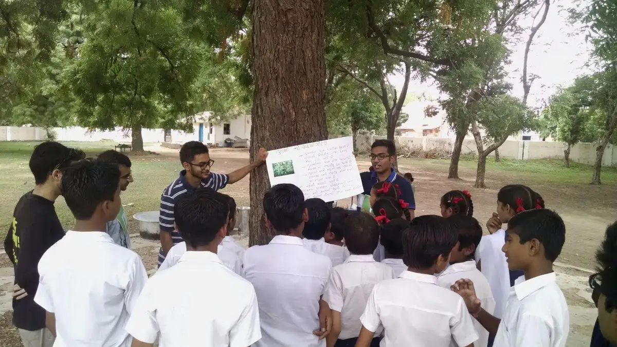 High school electrical engineering internship field work. Earth5R volunteers explaining a chart to school students under a tree