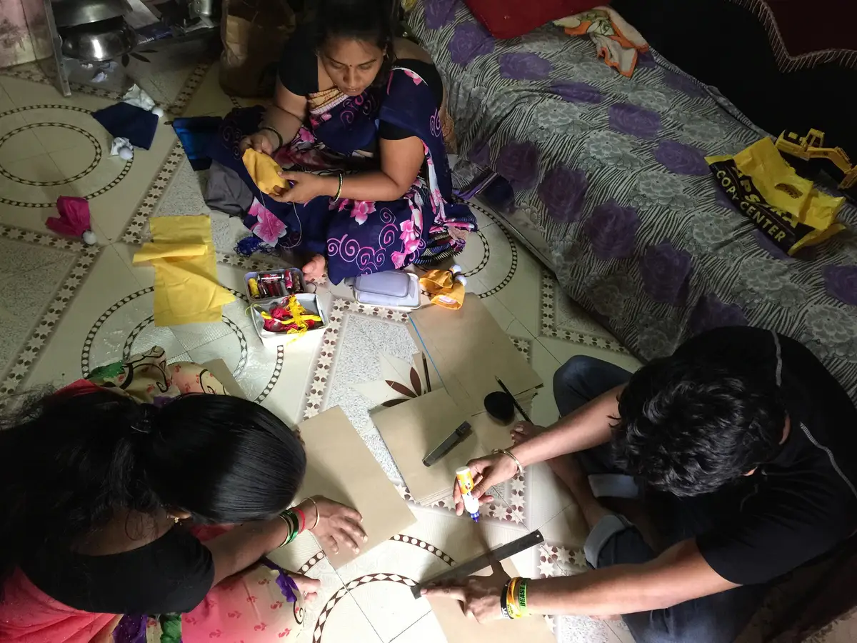 Woman and volunteers cutting and folding paper to make bags at home, Earth5R CSR programme in Mumbai