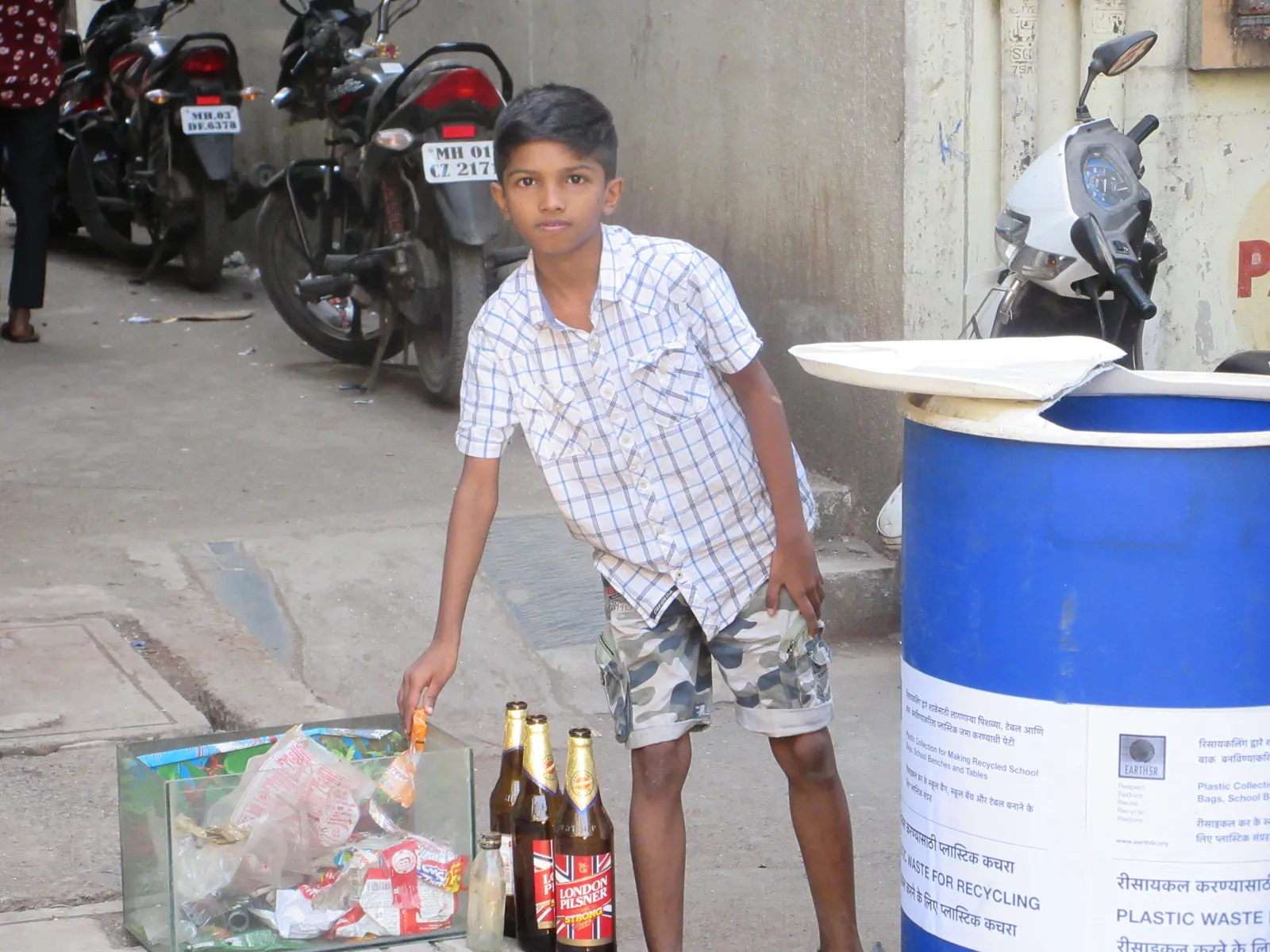 High school psychology internship field work. Boy putting plastic waste into a blue drum labelled Plastic Waste for Recycling in a parking lane
