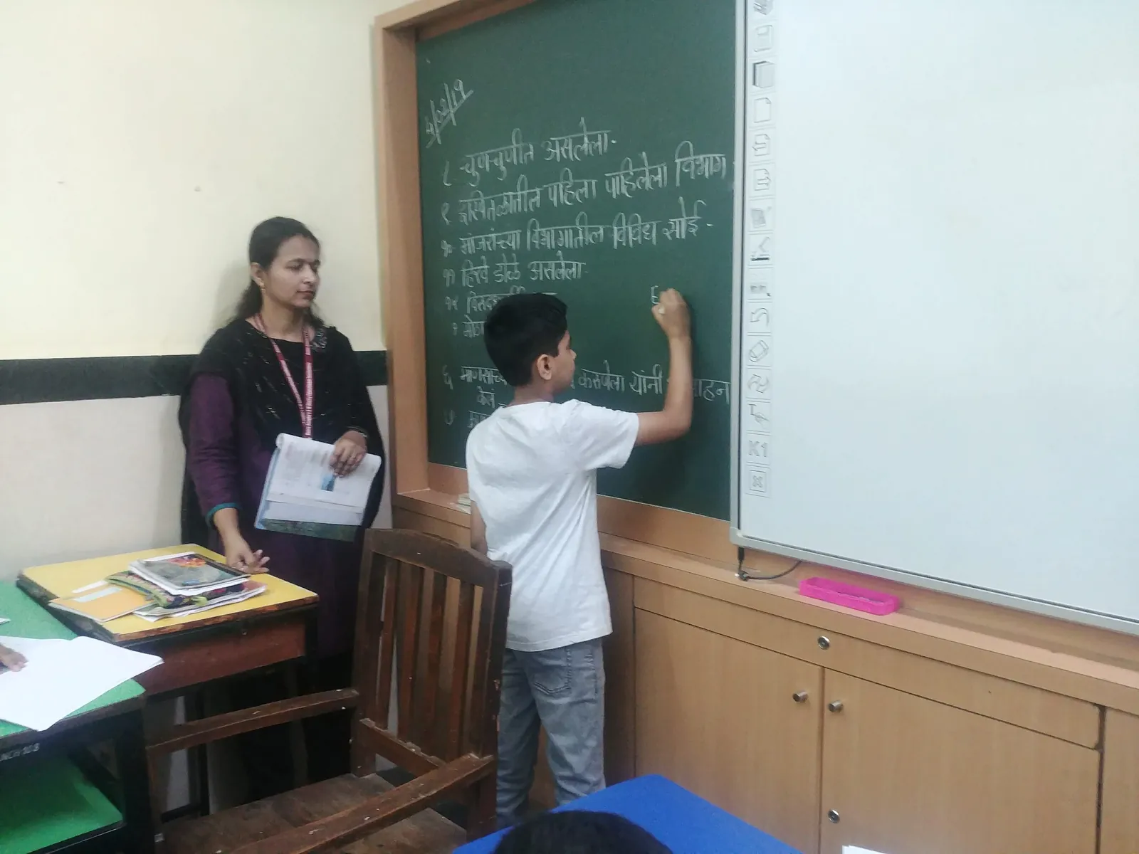 High school teaching internship field work. Boy writing on the blackboard during an Earth5R classroom session as the teacher watches