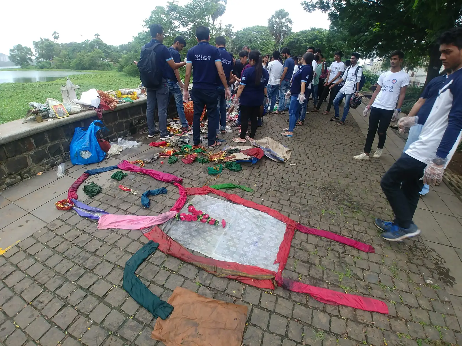 Collected waste laid out on paving by category for a brand and waste audit, volunteers around