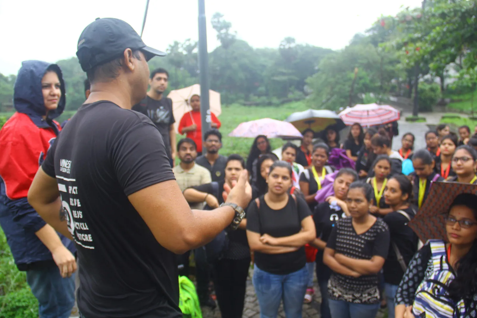 Content creation internship field work. Earth5R lead briefing a crowd of young volunteers with umbrellas before a monsoon lake cleanup