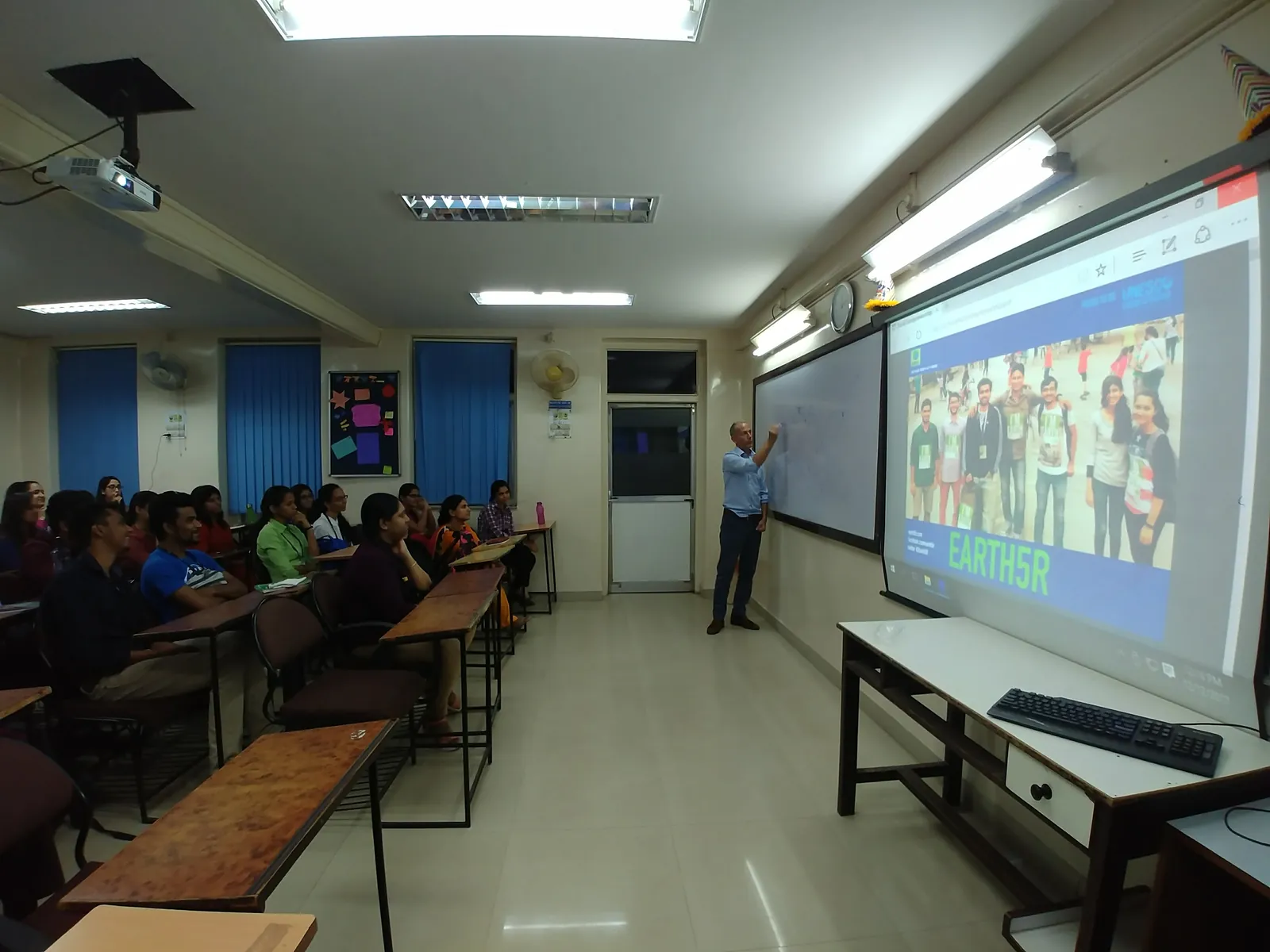 Students at benches watching a projected environment presentation in a classroom