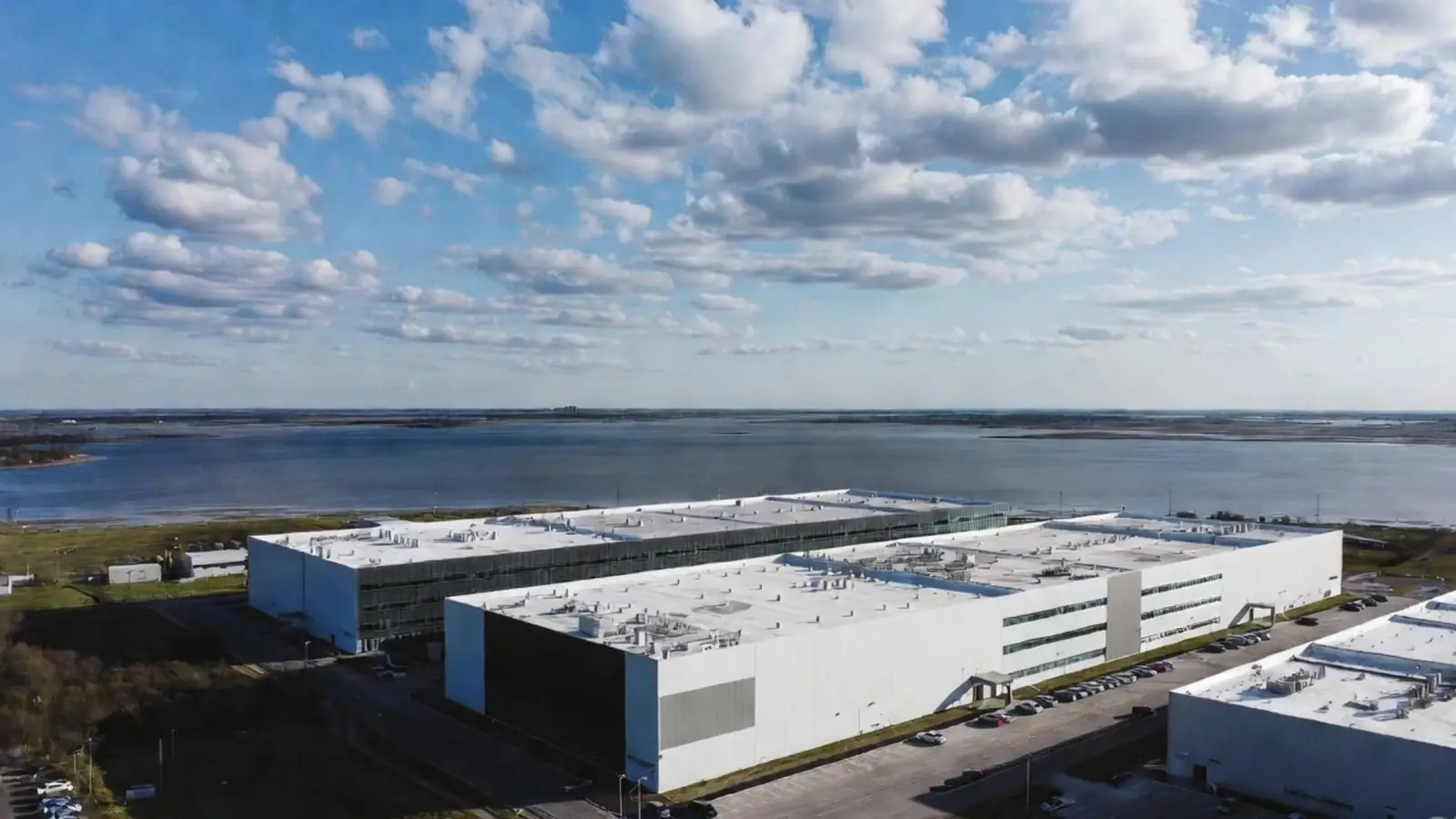 Aerial view of large white hyperscale data centre buildings on a coastline beside a bay, where seawater can be used for cooling instead of freshwater