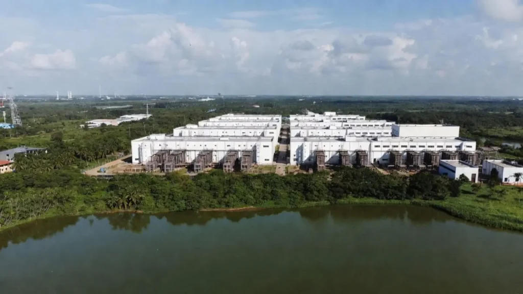 White data centre campus with external cooling equipment beside a lake, surrounded by palms, in a hot climate with high cooling water demand