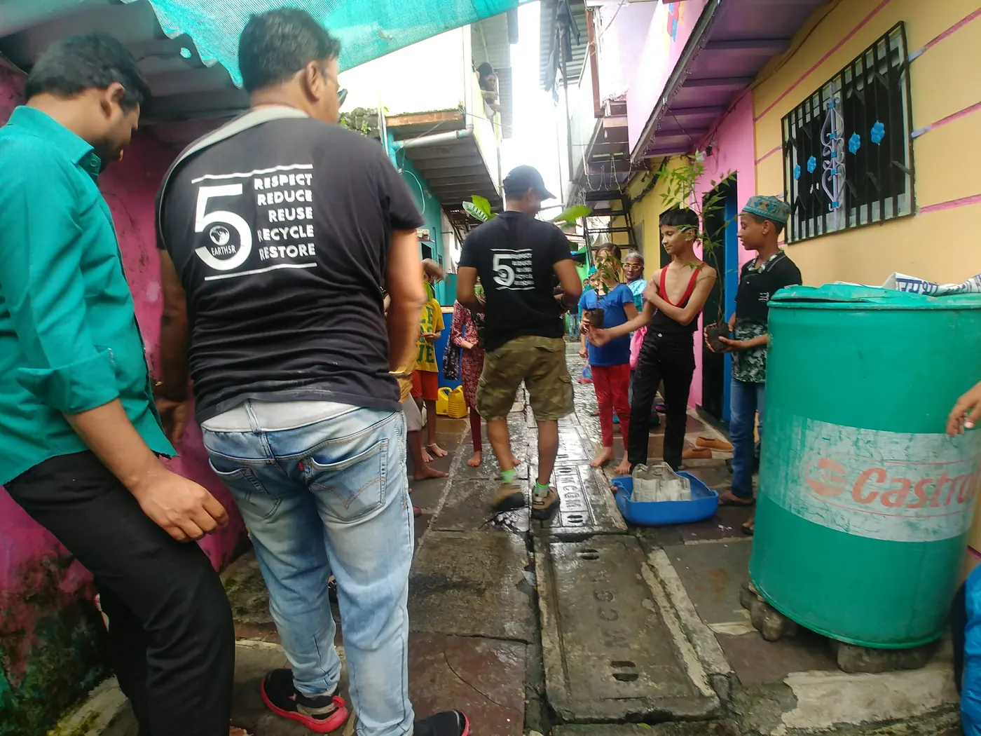Earth5R volunteers in black T-shirts printed with Respect, Reduce, Reuse, Recycle, Restore, beside a green water drum in a residential lane, 2018
