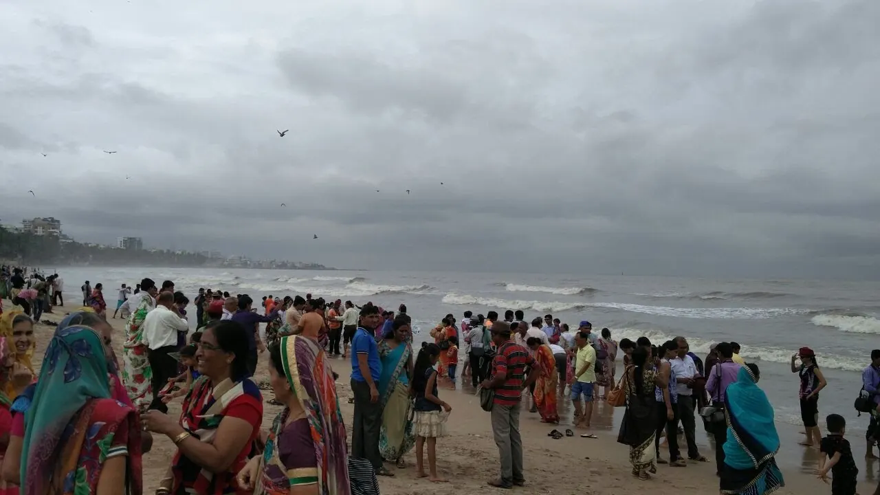 A large crowd of volunteers spread out along a grey beach under monsoon clouds during a mass beach cleanup