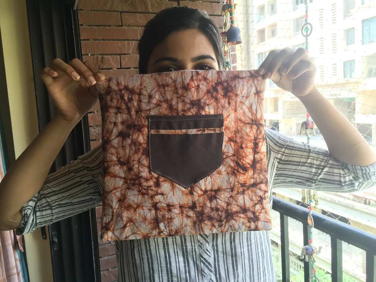 A woman on a balcony holding up a cloth pouch with a dark pocket, stitched from printed fabric at an Earth5R upcycling session, 2016