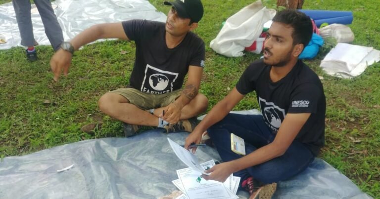 Two Earth5R volunteers sit on a tarp in a park sorting and recording waste audit data sheets during a field survey