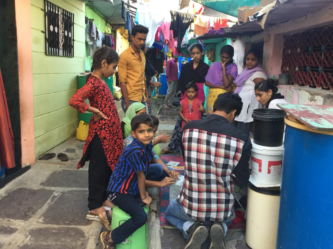 Earth5R volunteer sitting with residents and children in a narrow lane lined with blue and white water storage drums, 2017