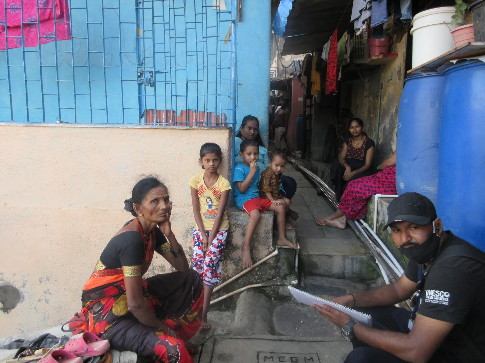 High school public health internship field work. Earth5R volunteer sitting with a woman at her doorstep to fill in a household survey form