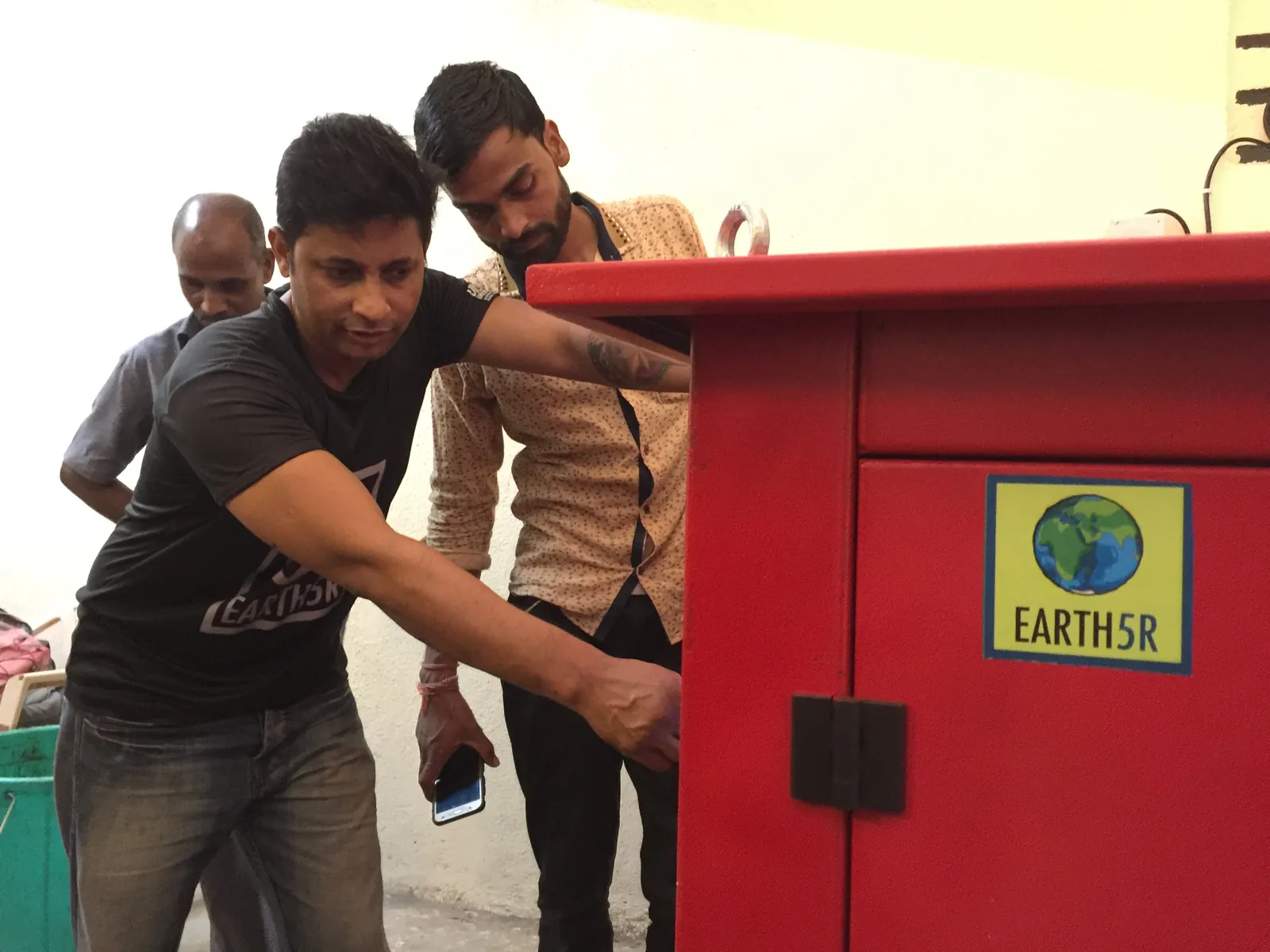 Two men inspecting a red composting machine with an Earth5R sticker