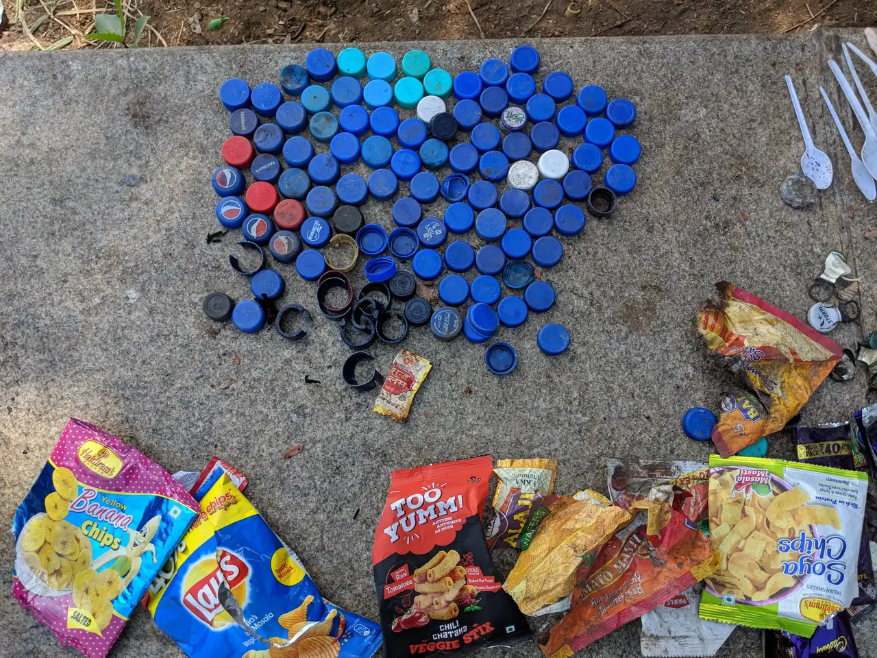 High school finance internship field work. Collected bottle caps and snack wrappers laid out on concrete for a brand and waste audit in Powai Lake, Mumbai