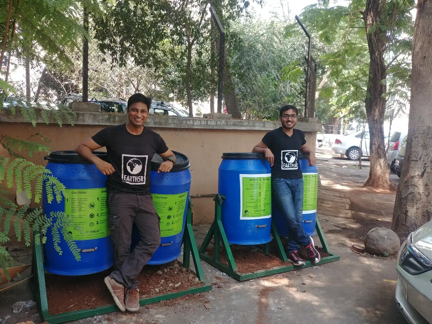 High school environmental engineering internship field work. Two Earth5R team members beside blue and green compost drums in a housing society garden in Powai, Mumbai