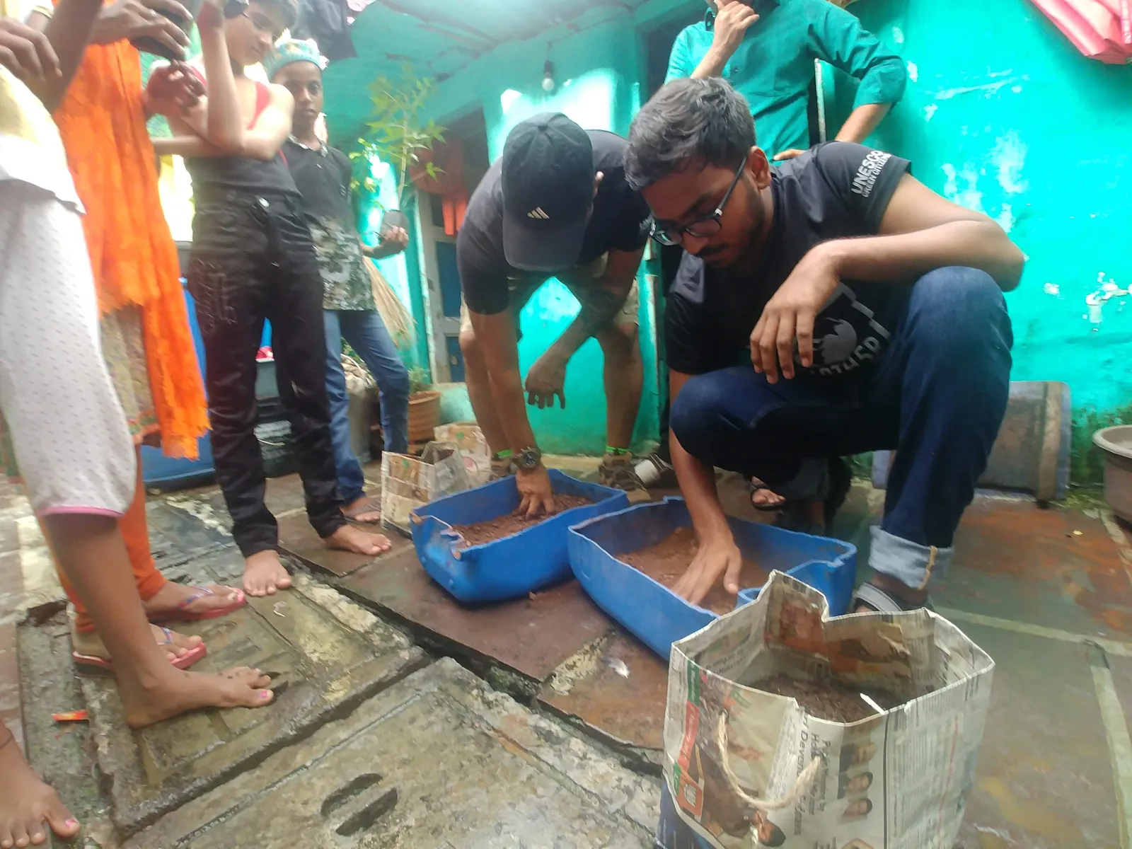 High school chemical engineering internship field work. Earth5R volunteers demonstrating composting in blue trays to residents in Mumbai