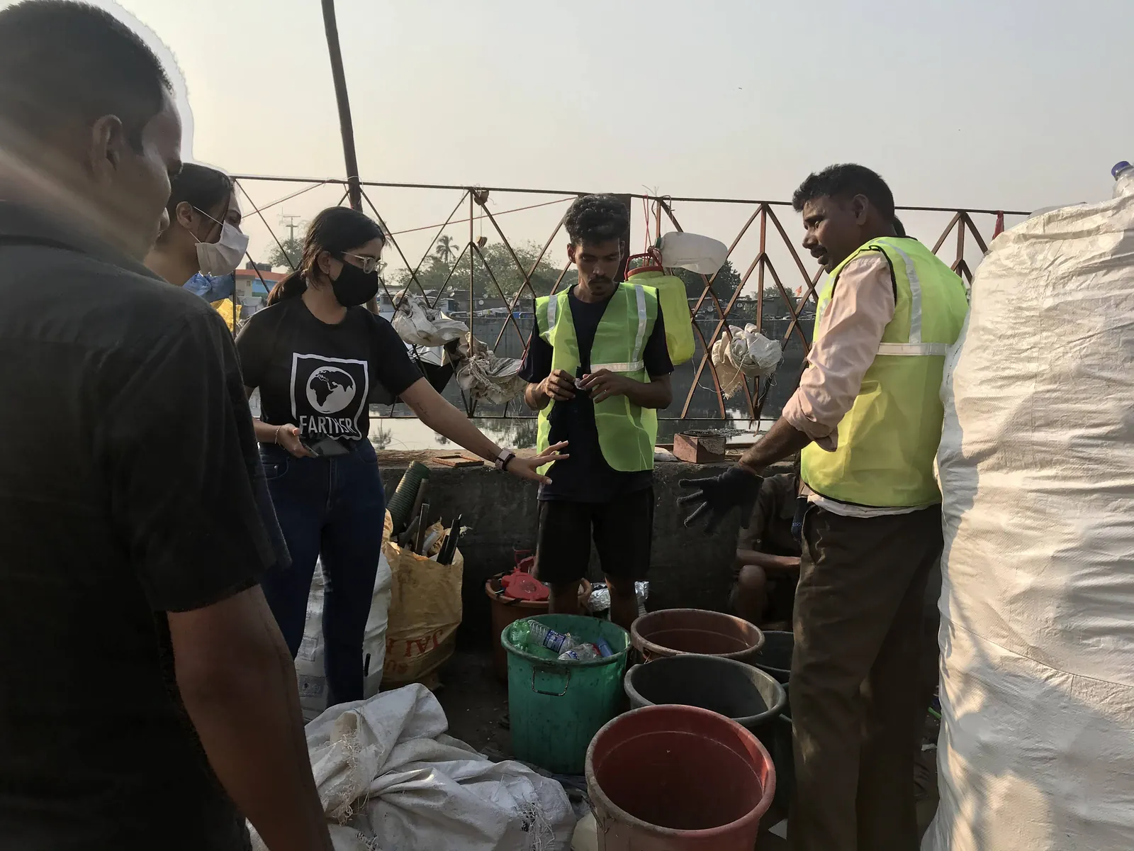Volunteers and workers in hi-vis vests around buckets of sorted waste at a dry waste centre in Mithi River, Mumbai