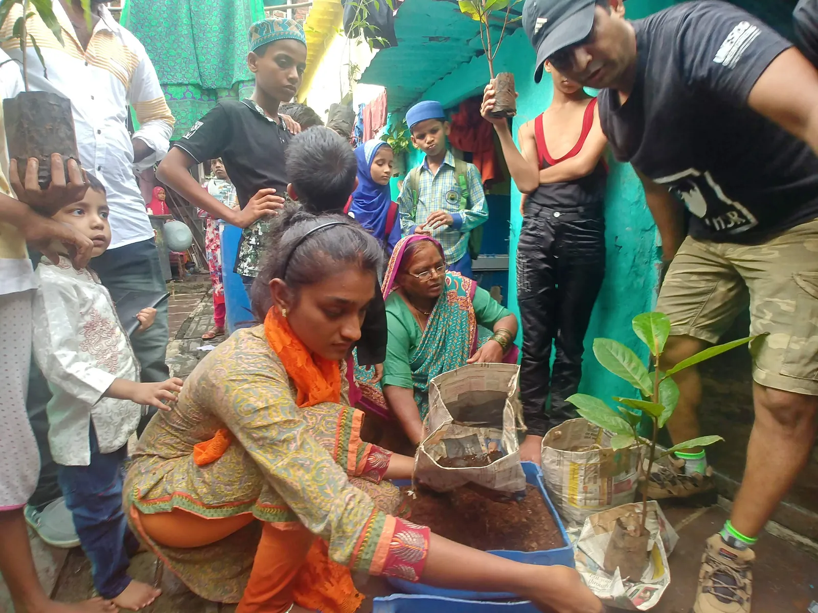 Woman in an orange sari planting saplings in blue crates with Earth5R volunteers in Mumbai