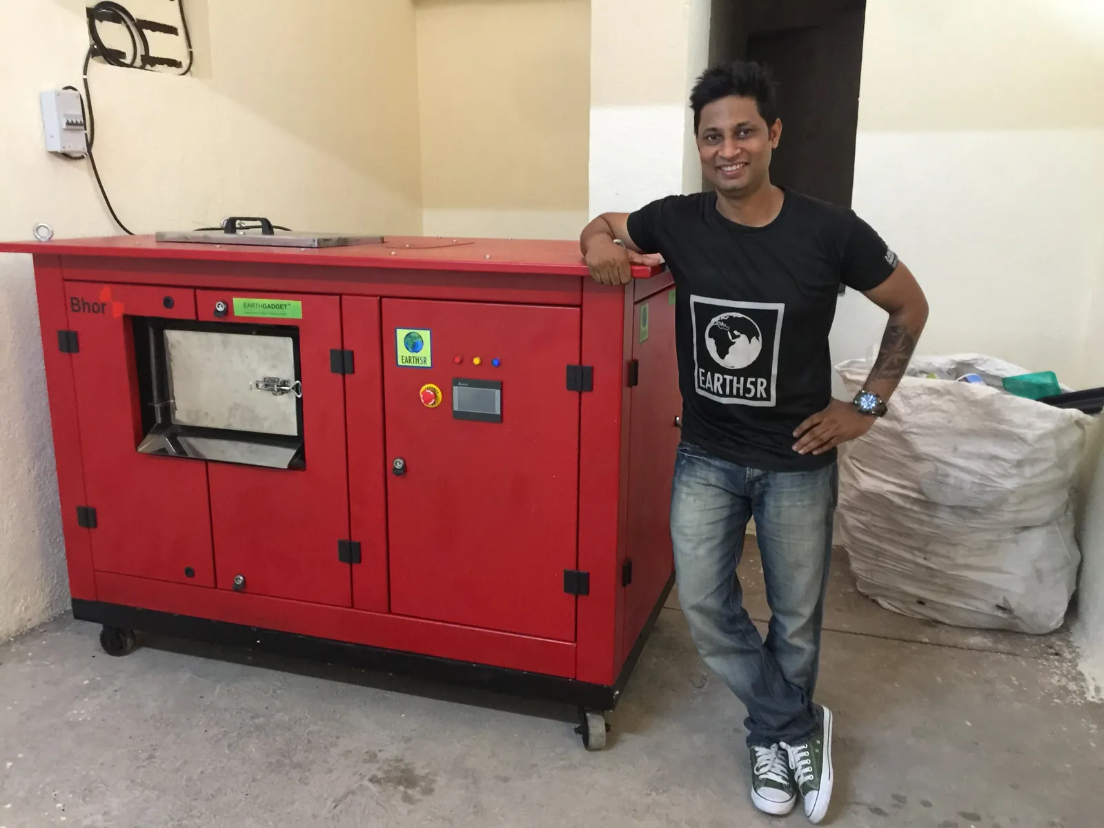 Earth5R volunteer beside a red organic waste composting machine and sacks of wet waste